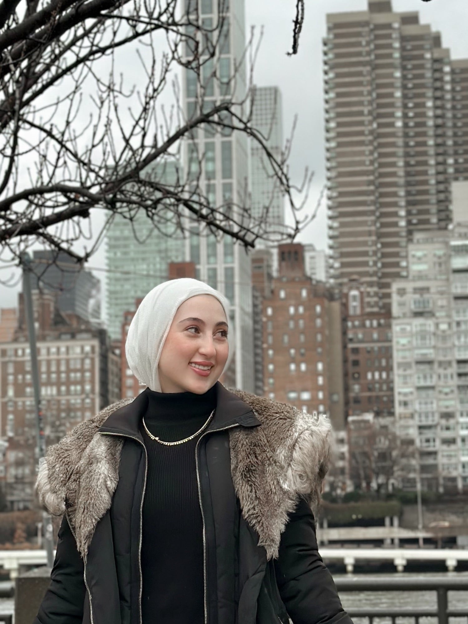 Farah Olabi, founder and lead photographer of Veil & Light, photographed along the East River with the Manhattan skyline behind her
